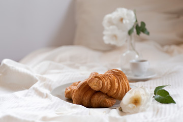 Obraz na płótnie Canvas Croissants in bed with espresso in cup and white roses in vase. Horizontal with copy space.