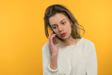 The young girl is talking on the phone, she is with her hair, in a white jacket, on a yellow background