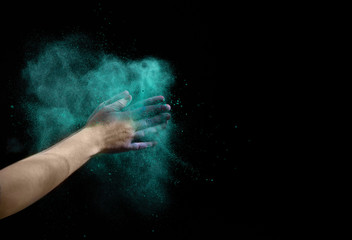 Fototapeta na wymiar Cloud of dry blue paint around hands on black background