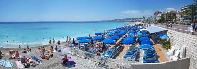 Fototapeta na wymiar Nizza Strand mit blauen Schirmen im Sommer Panorama