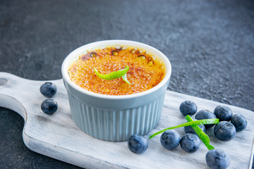 Creme brulee - traditional french vanilla cream dessert with caramelised sugar on top, blueberries and lime pile on rustic white wooden board, dark table. Sweet dessert -custard. Copy space.