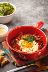 shakshuka in a red pan, coffee, bread  and salad in a bowl, gray background, copy space