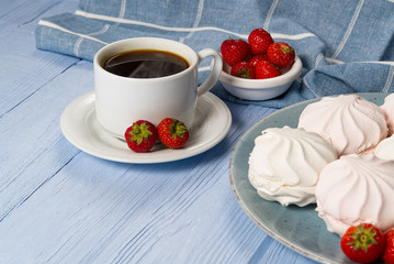 Cup of americano coffee and homemade zephyr or marshmallow in a blue plate on light blue wooden background.