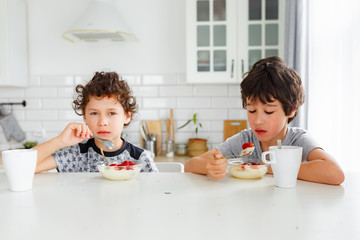 eal brothers have breakfast in the morning in a bright Scandinavian style kitchen with porridge with strawberries