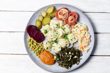 Dumplings surrounded by various appetizers on gray plate on white wooden background