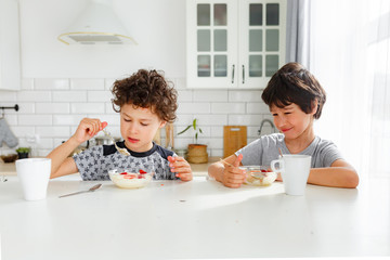 eal brothers have breakfast in the morning in a bright Scandinavian style kitchen with porridge with strawberries