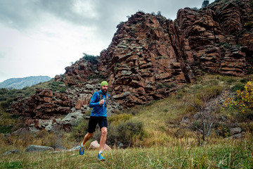 Athlete runs high in the mountains among the rocks. Bearded guy jogging in the mountains. Trail...