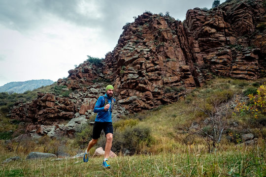 Athlete runs high in the mountains among the rocks. Bearded guy jogging in the mountains. Trail running