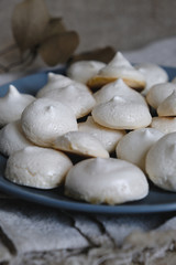 Fototapeta na wymiar Homemade meringue cookies closeup. Tasty white baked meringues with texture and cracks in the foreground on blue plate