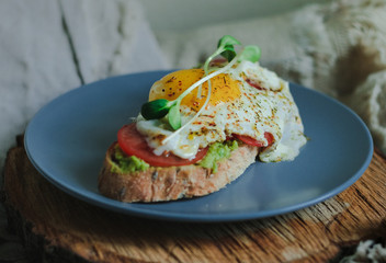 Healthy avocado toast. Sandwich with avocado, tomato and poached egg on wooden board. Delicious breakfast or snack