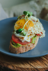 Avocado toast with tomato and poached egg. Healthy sandwich on wooden board. Delicious breakfast, brunch or snack