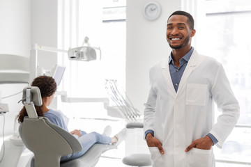 Confident black dentist standing next to female patient in chair