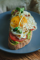 Avocado toast on wooden board. Delicious breakfast, brunch or snack. Healthy sandwich with tomato and poached egg