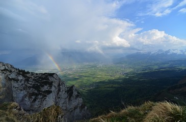 rainbow with rock wall in the foreground and in the background the river Rhine in the valley and the principality of Liechtenstein