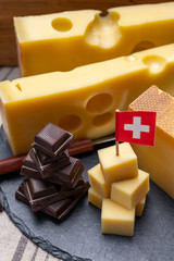 Tasty Swiss food, block of medium-hard yellow cheese emmental or emmentaler with round holes, matured gruyere and high quality milk chocolate served in cubes as mountains top with Swiss flag.