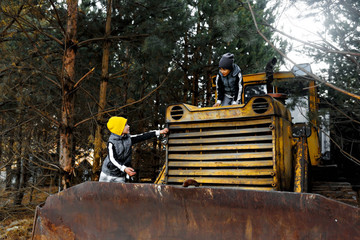 Two boys in sportswear, real brothers, climbed onto a yellow bulldozer that stands in the pines. © Olga Gimaeva