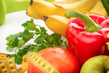 fruits and vegetables with dumbbells and measuring tape on a white background, healthy food, peppers, bananas, Apple, greens,  tomato,