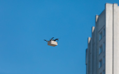 Modern electro drone with the cardboard box flying over the town