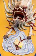 Fengdu, China - May 8, 2010: Yangtze River boat terminal gate. Closeup of head and pool of saliva of beige dragon with violent manes and teeth on yellow backdrop, set in wall.