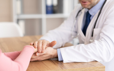 Portrait of mature doctor holding female patient's hands