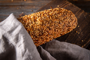 loaf of fresh grain bread on a gray towel on a dark wooden background close-up, food, top view