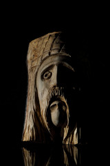 Warrior head sculpted on a wooden log with black background and side light