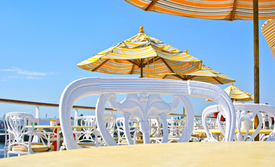 Outdoor bistro or cafe with iron cast chairs and sun umbrellas in yellow colors against blue sky on...