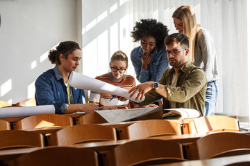 Group of design students sitting in classroom and examining blueprint homework project.	
