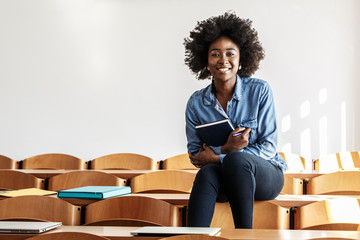 In the university classroom, a portrait of determined black female student sits alone, absorbed in her test, showcasing her academic prowess and dedication to her studies.
