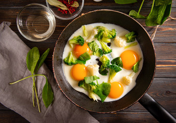fried eggs with broccoli and spinach in a pan on a dark wooden , Breakfast