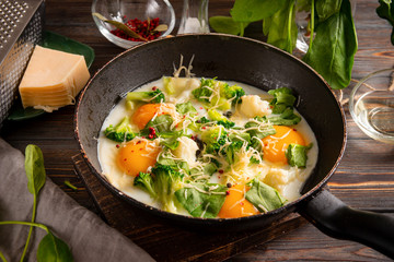 4 fried eggs with broccoli, spinach, spices and cheese in a pan on a dark, Breakfast