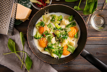 fried eggs with broccoli, spinach, spices and cheese in a pan on a dark wooden background, Breakfast