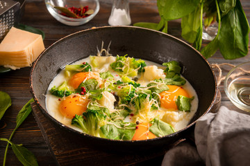 fried eggs with broccoli, spinach, cheese  and spices  in a pan on a dark wooden background, healthy . Breakfast