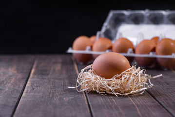 A fresh egg on the straw, with a full package of eggs in the background. Wooden background. Copy space. Space for text.