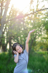 Young girl is dancing and listening the music till walking in the park. Musical cheerful mood. A little girl listens to music on headphones. Child girl in big headphones enjoys the music.
