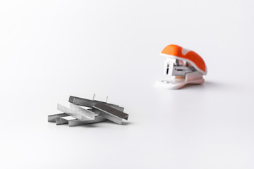 A small orange stapler and staples on a white background. Close-up. Copy space. Space for text