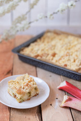 Kuchen mit Rhabarber und Streusel aus einem Blech auf einem Tisch aus hellem Holz