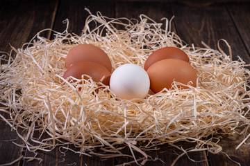 Fresh chicken eggs in a nest of hay on a wooden background.