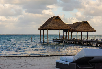 lounge chair on a beach with two palapas, traditional Mexican shelter with thatched roof of palm leaves 
