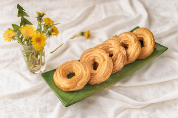 Eclair rings with cream in a green plate and bouquet of spring flowers, light background. Spring, sweet food concept