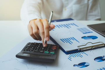 Close-up hand of businessman holding a pen and using a calculator to calculate the numbers, tax and analyze graph chart and business data on the white desk in the office. finance accounting concept.
