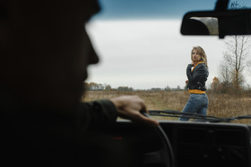 Woman standing in front of the car and man silhouette looking at her