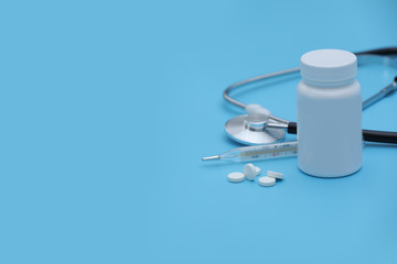 Pills spilling out of pill bottle syringe thermometer and stethoscope on blue background