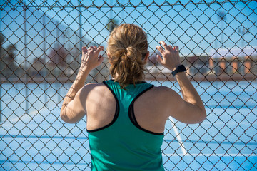 Sportwoman from back leaning against the fences and looking at a tennis court. sports