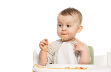 Portrait of funny baby boy that eats spaghetti in tomato sauce on white isolated background.