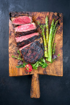 Gegrilltes dry aged Wagyu Entrecote Steak von Rind mit Salat und grünen Spargel als Draufsicht auf einem alten rustikalen Holz Schneidebrett