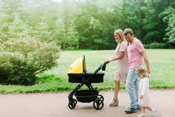 family with a stroller walking in the park on a summer day, family on the weekend