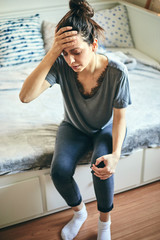 Woman suffering from knee pain while sitting on bed.