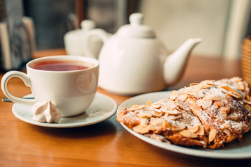 Close up of tea cup, teapot and croissant on table in cafe