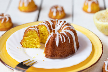 kleiner gelber kuchen bzw gugelhupf aus zitronen mit zuckerguss auf weißem tisch aus brettern und holz